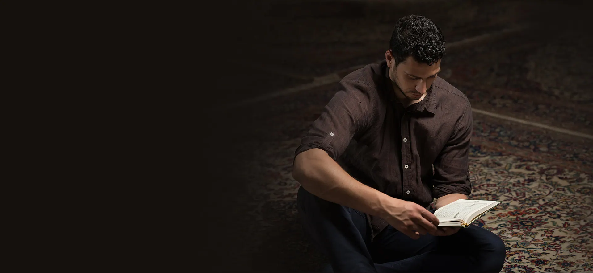 A man reading the Qur’an on a patterned carpet